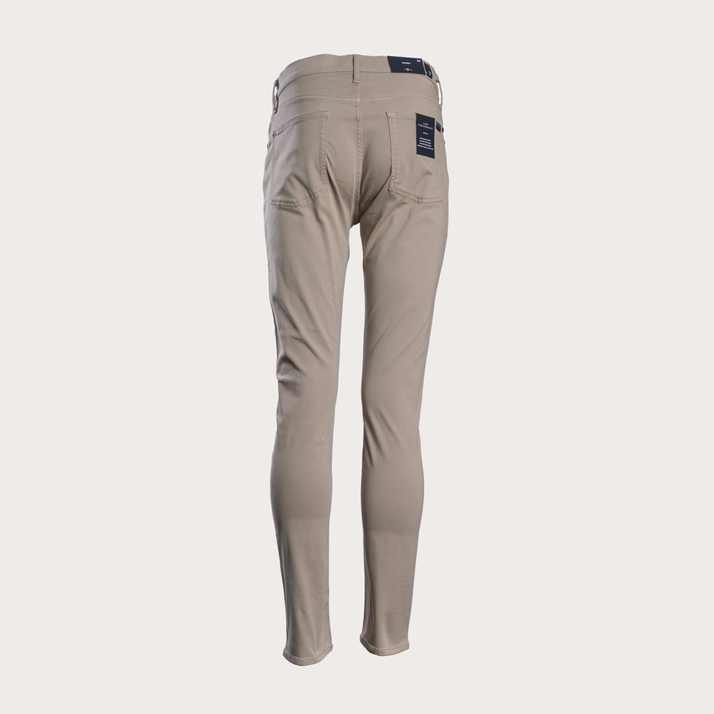 A pair of slim-fit, straight-leg pants in a light taupe-beige color, shown against a solid off-white background. 7 For All Mankind Slimmy Sateen Jeans. Sakks Menswear Southampton.