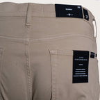 Close-up of the back waistband and pocket area of beige slim-fit trousers, showing a black fabric brand label at the back waistband and a black back pocket patch reading Luxe Performance. 7 For All Mankind. Sakks Menswear Southampton.