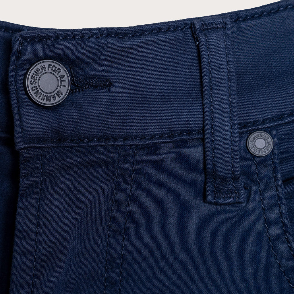 A detailed close up of a pair of jeans in a deep navy Colour. The image shows the belt loop and waistband of a pair of 7 For All Mankind Slimmy Sateen Jeans. The button reads "Seven For All Mankind". Sakks Menswear Southampton