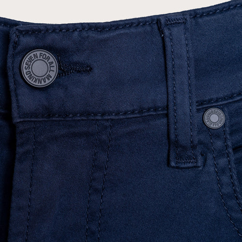 A detailed close up of a pair of jeans in a deep navy Colour. The image shows the belt loop and waistband of a pair of 7 For All Mankind Slimmy Sateen Jeans. The button reads "Seven For All Mankind". Sakks Menswear Southampton