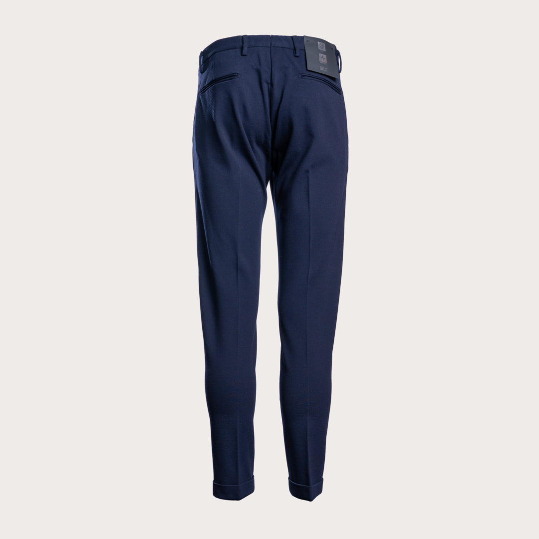 A pair of navy blue trousers shown from the back, featuring a clean silhouette with a small dark brand patch on the back waistband, set against a solid light gray background. Briglia 1949 Trousers available at Sakks Menswear in Southampton.