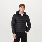 A man wearing a black hooded puffer jacket with a full-zip front, ribbed cuffs and hem, and a white t-shirt underneath, standing against a light grey studio background. Belstaff Down Jacket. Sakks Menswear Southampton.