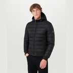 A man wearing a black hooded puffer jacket with a full-zip front, ribbed cuffs and hem, and a small yellow embroidered logo patch on the left sleeve, photographed against a plain light grey studio background. Belstaff Down Jacket. Sakks Menswear Southampton.