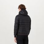 A man viewed from the back wearing a black hooded puffer jacket with horizontal quilting and a small tan logo patch on the upper left sleeve, set against a plain white studio background. Belstaff Down Jacket. Sakks Menswear Southampton.