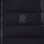 Close-up of a black puffer vest showing the central zip closure and a dark gray rectangular Beaufort brand patch on the chest. Belstaff Gilet. Sakks Menswear Southampton.