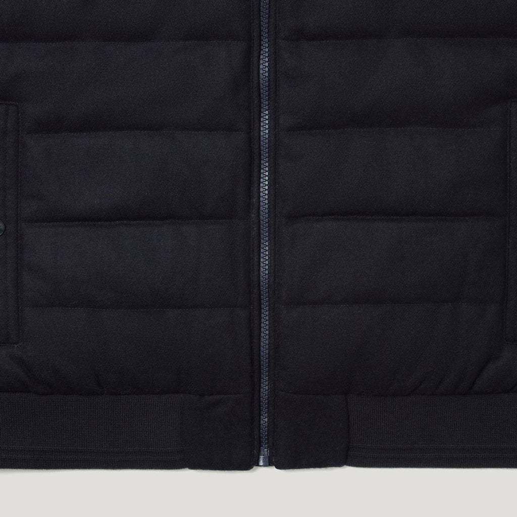 Close-up of a black quilted puffer jacket showing horizontal stitching, a central zipper, and ribbed knit trim at the bottom. Belstaff Gilet. Sakks Menswear Southampton.