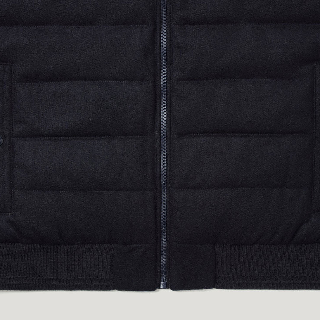Close-up of a black quilted puffer jacket showing horizontal stitching, a central zipper, and ribbed knit trim at the bottom. Belstaff Gilet. Sakks Menswear Southampton.
