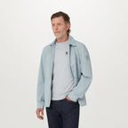 A man wearing a light blue lightweight jacket over a light gray t-shirt and dark blue jeans, standing against a plain white studio background. Belstaff T-Shirt. Sakks Menswear Southampton.