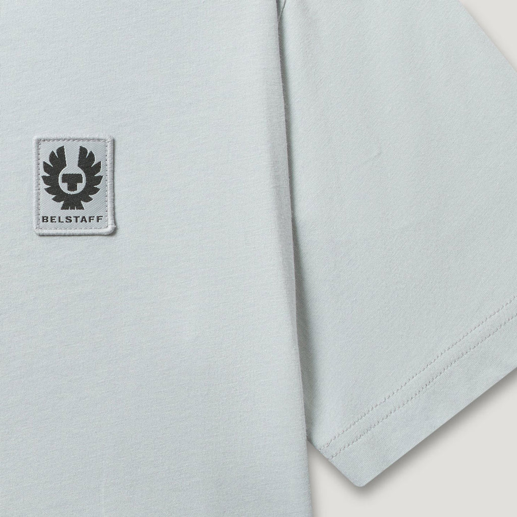Close-up of a light gray short-sleeve T-shirt with a square Belstaff logo patch on the chest and a visible hem seam. Belstaff T-Shirt. Sakks Menswear Southampton.
