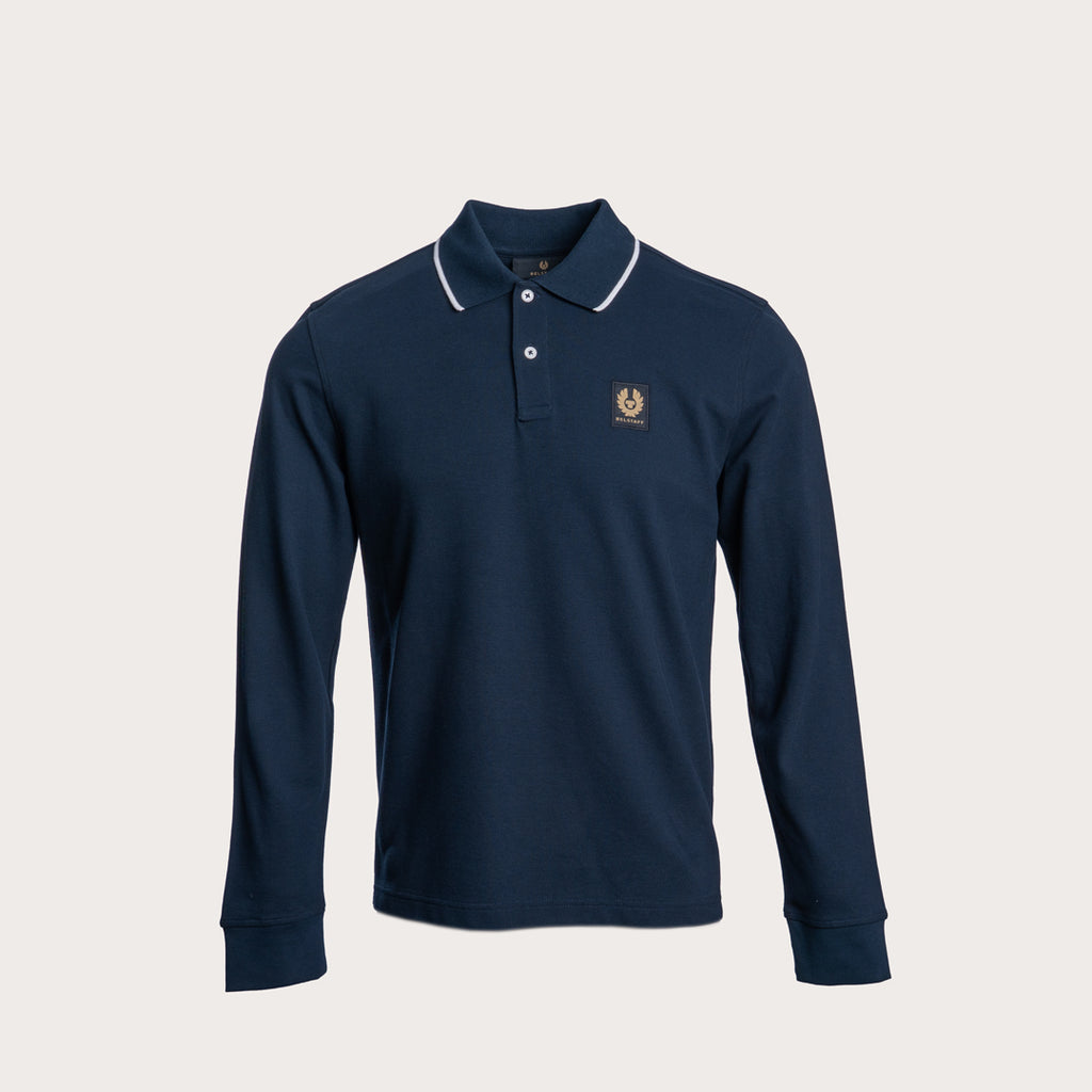 A navy blue long-sleeve polo shirt shown from the front, featuring a thin white stripe detail along the collar, set against a solid light beige background. Belstaff Long Sleeved Polo. Sakks Menswear Southampton.