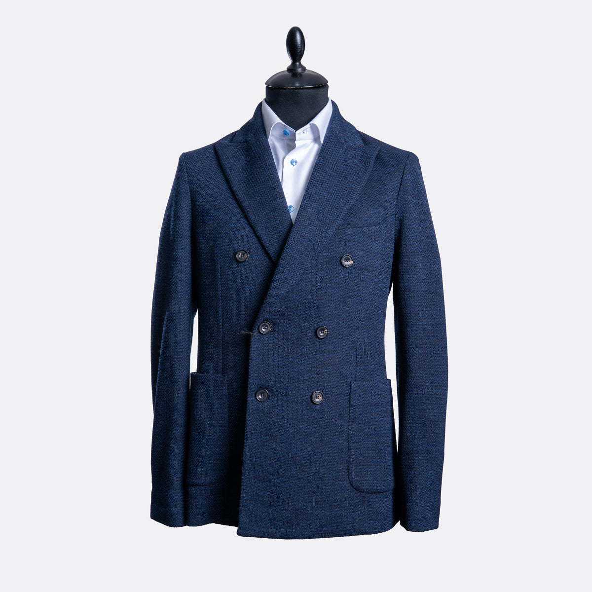 A men's double-breasted blazer in textured navy blue, displayed on a black mannequin torso with a light blue dress shirt underneath, set against a plain light gray background. Circolo 1901 Blazer available at Sakks Menswear in Southampton.