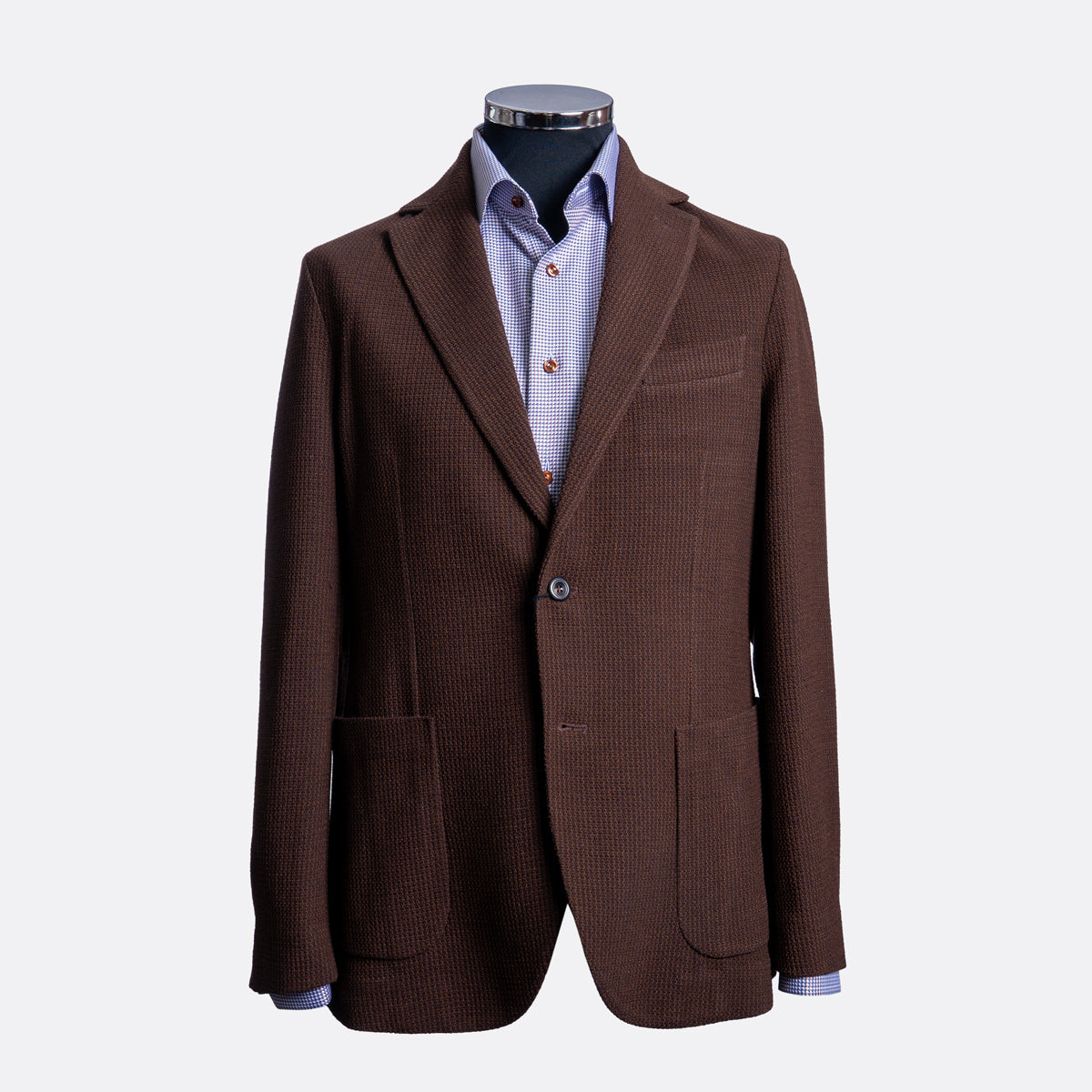 A brown textured blazer jacket displayed on a mannequin torso, layered over a light blue and white checkered dress shirt, against a plain light gray background. Circolo 1901 Blazer available at Sakks Menswear in Southampton.