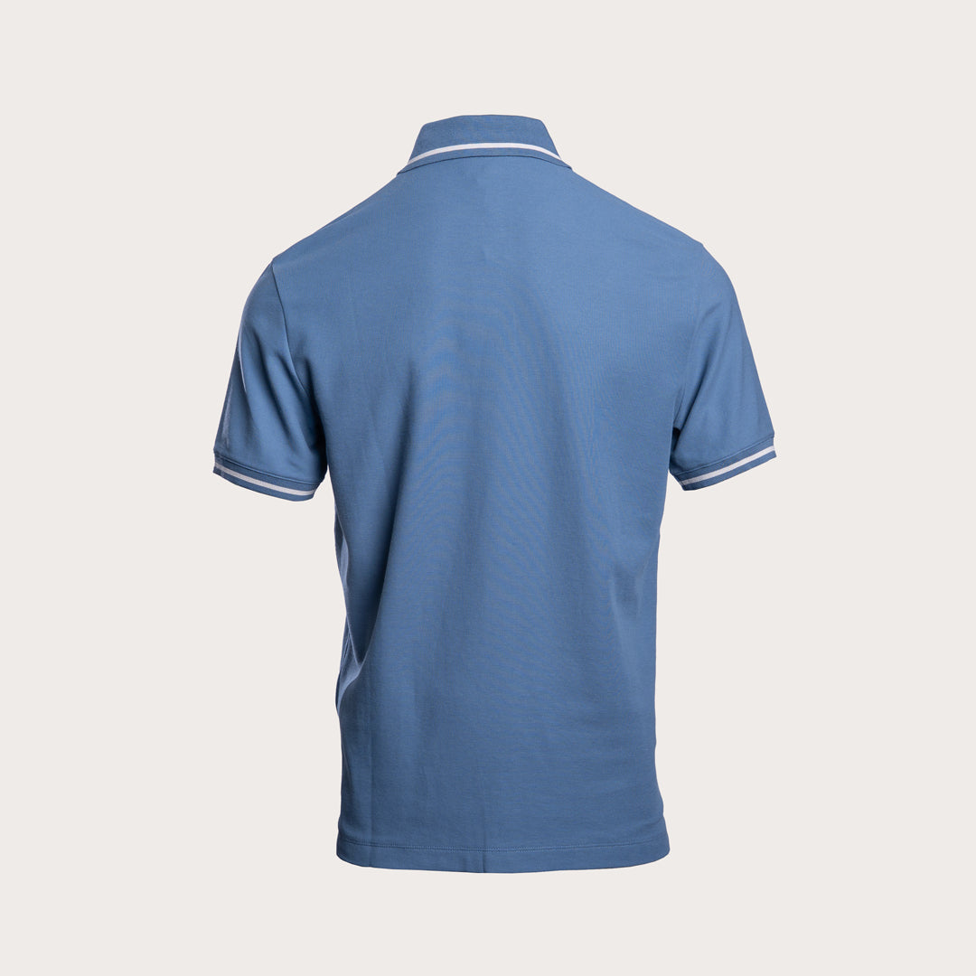 A blue short-sleeve polo shirt shown from the back, featuring white contrast stitching on the collar and sleeve cuffs, set against a solid light beige background. Emporio Armani Polo. Sakks Menswear Southampton.