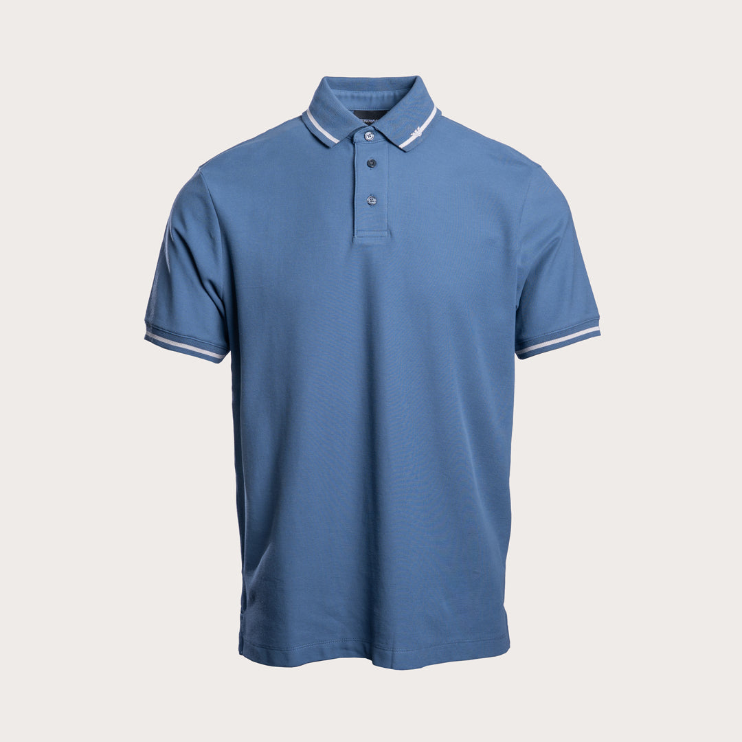 A blue short-sleeve polo shirt with white contrast stitching on the collar and sleeve cuffs, displayed against a light beige background. Emporio Armani Polo. Sakks Menswear Southampton.