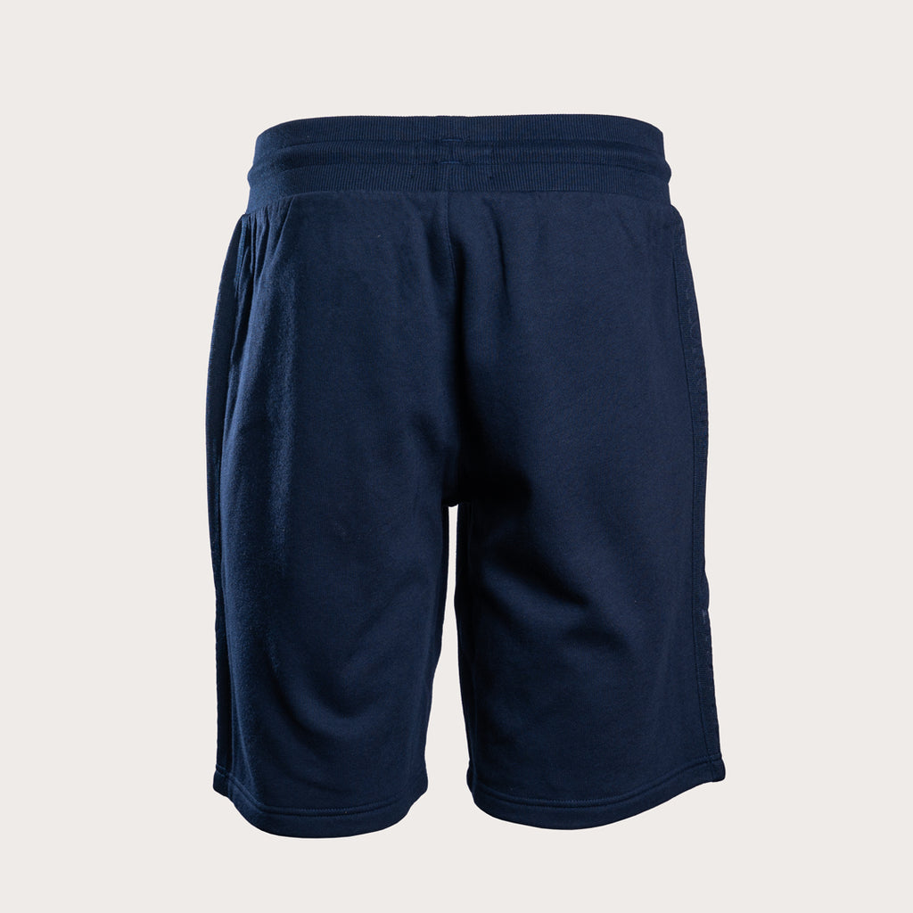 A pair of dark navy blue athletic shorts with an elastic waistband, shown from the back on a light beige background. Emporio Armani Shorts. Sakks Menswear Southampton.