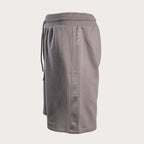 A pair of gray sweat shorts featuring a vertical tonal 'EMPORIO ARMANI' logo print down the left leg and a matching drawstring waist, shown against a light beige background. Emporio Armani Sweat Shorts. Sakks Menswear Southampton.