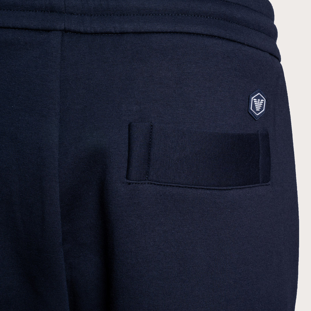 Close-up of navy blue sweatpants showing the back pocket with a hook-and-loop closure and a small embroidered shield logo on the upper back. Emporio Armani Sweat Pants. Sakks Menswear Southampton.