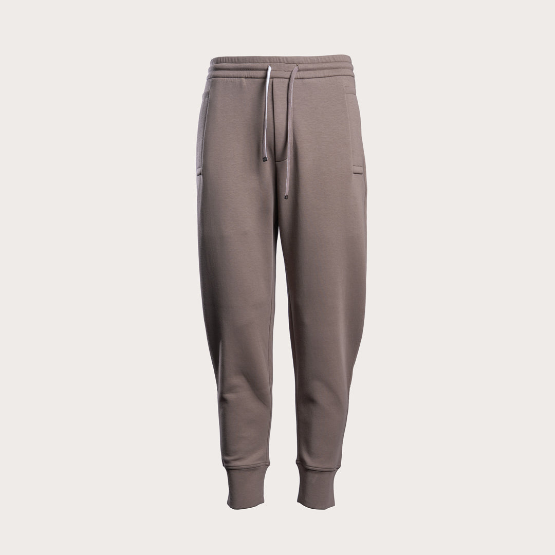 A pair of men's jogger sweatpants in a muted taupe-brown color, featuring an elastic waistband with a white drawstring, side pockets, and ribbed ankle cuffs, shown against a solid light gray background. Emporio Armani Sweat Pants. Sakks Menswear Southampton.