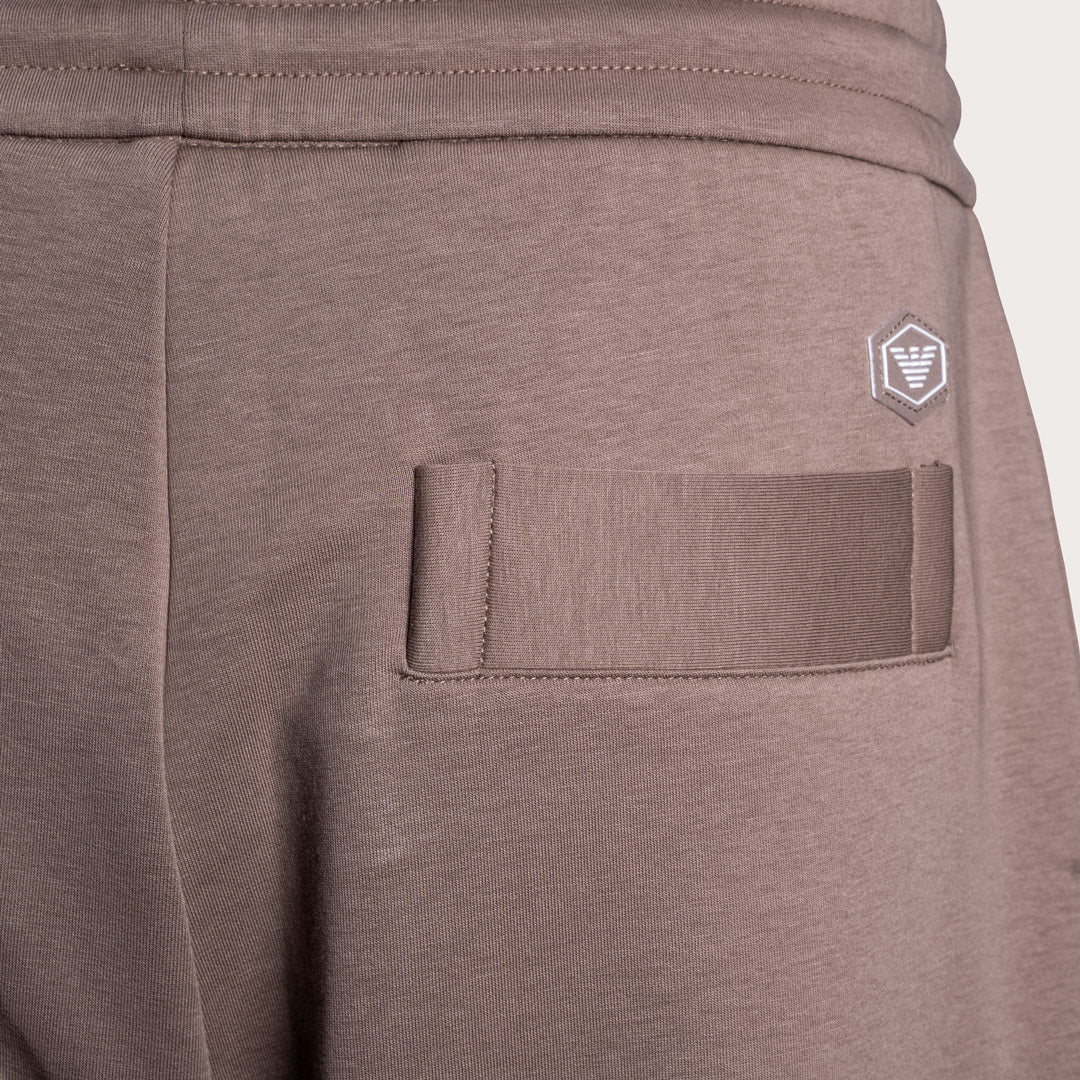 Close-up of a pair of heather taupe sweatpants showing the back pocket and a small white embroidered shield logo on the upper right side. Emporio Armani Sweat Pants. Sakks Menswear Southampton.