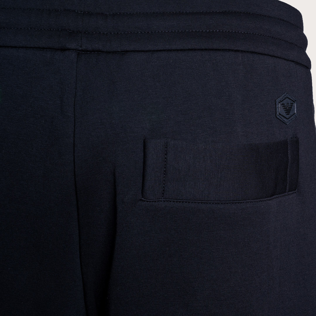 Close-up of dark navy athletic sweatpants showing a side pocket with a tonal embroidered logo on the upper right side. Emporio Armani Sweat Pants. Sakks Menswear Southampton.