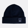 A dark navy blue knit beanie hat with a folded cuff, featuring a small white embroidered Emporio Armani eagle logo patch on the right side of the cuff, set against a light gray background. Emporio Armani Beanie. Sakks Menswear Southampton.
