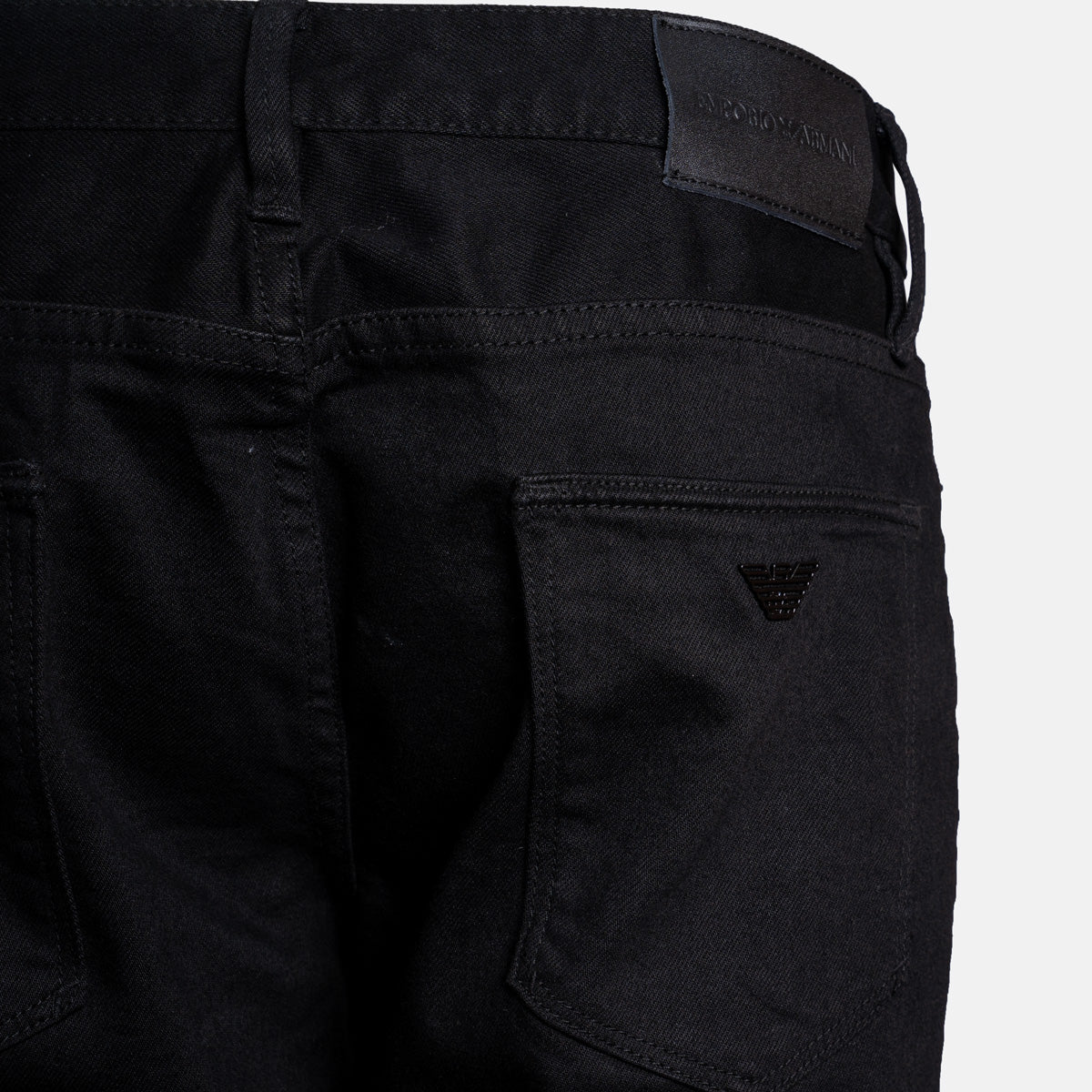 Close-up of the back waistband and right rear pocket of black Emporio Armani jeans, showing the brand patch and logo. Emporio Armani Jeans. Sakks Menswear Southampton.