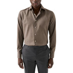 A man wearing a brown long-sleeve button-down shirt and dark grey trousers, cropped from the mouth down against a plain white background. Eton Shirt available at Sakks Menswear in Southampton.