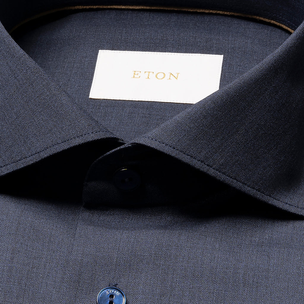 Close-up of a dark navy ETON dress shirt collar with a white neck label featuring gold lettering, and part of a blue button visible. Eton Shirt available at Sakks Menswear in Southampton.