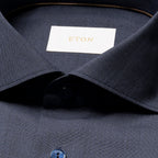 Close-up of a dark navy ETON dress shirt collar with a white neck label featuring gold lettering, and part of a blue button visible. Eton Shirt available at Sakks Menswear in Southampton.