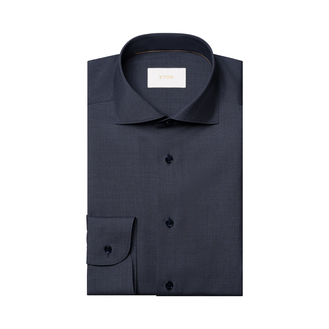 A folded dark navy blue dress shirt with a spread collar and button front, shown on a plain white background. A small white neck label is visible inside the collar. Eton Shirt available at Sakks Menswear in Southampton.