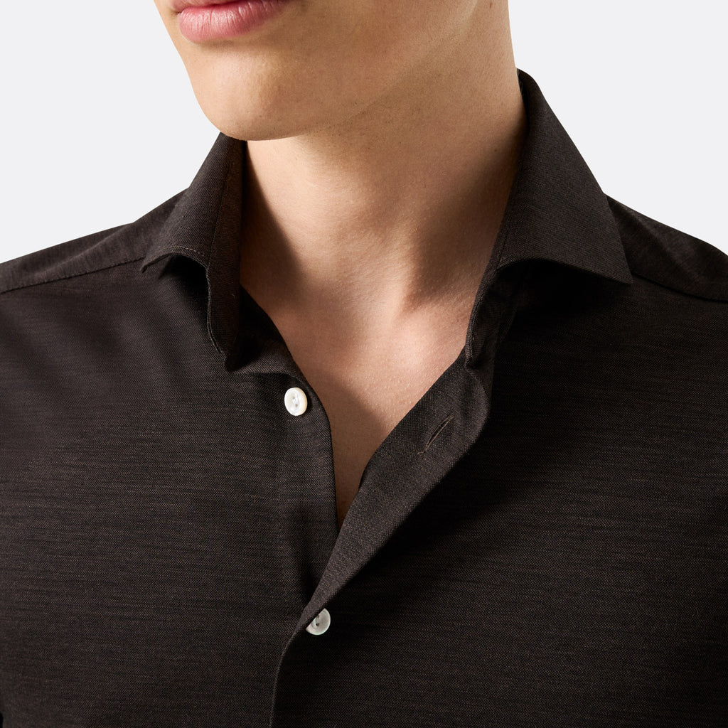 Close-up of a man wearing a dark brown textured button-down shirt, showing the collar, chest area, and part of his lower face against a light gray background. Eton Shirt available at Sakks Menswear in Southampton.