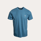 A blue short-sleeve crewneck t-shirt with a small white geometric logo on the left chest, displayed on a light beige background. MA.Strum T-Shirt available at Sakks Menswear in Southampton.