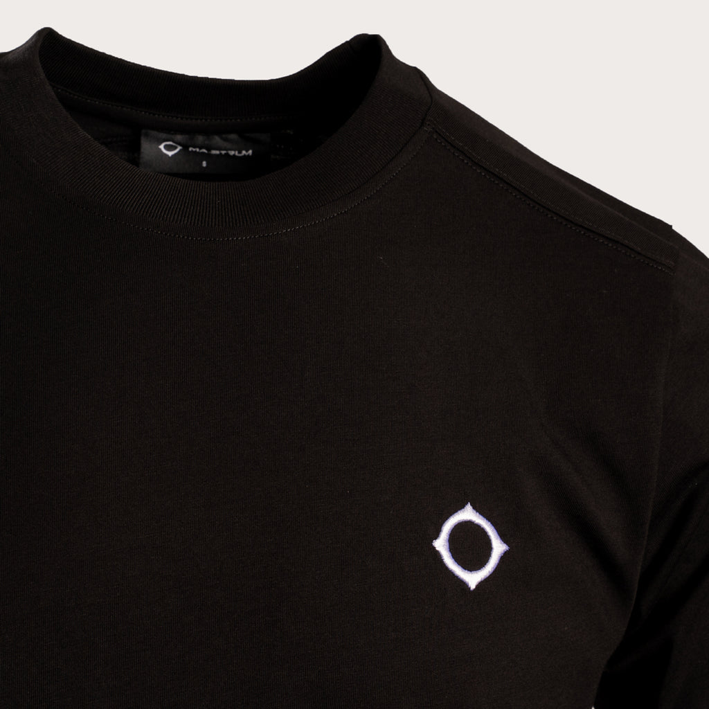 Close-up of a black crewneck sweatshirt featuring a small white geometric logo on the left chest, set against a light gray background. MA.Strum T-Shirt available at Sakks Menswear in Southampton