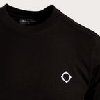 Close-up of a black crewneck sweatshirt featuring a small white geometric logo on the left chest, set against a light gray background. MA.Strum T-Shirt available at Sakks Menswear in Southampton