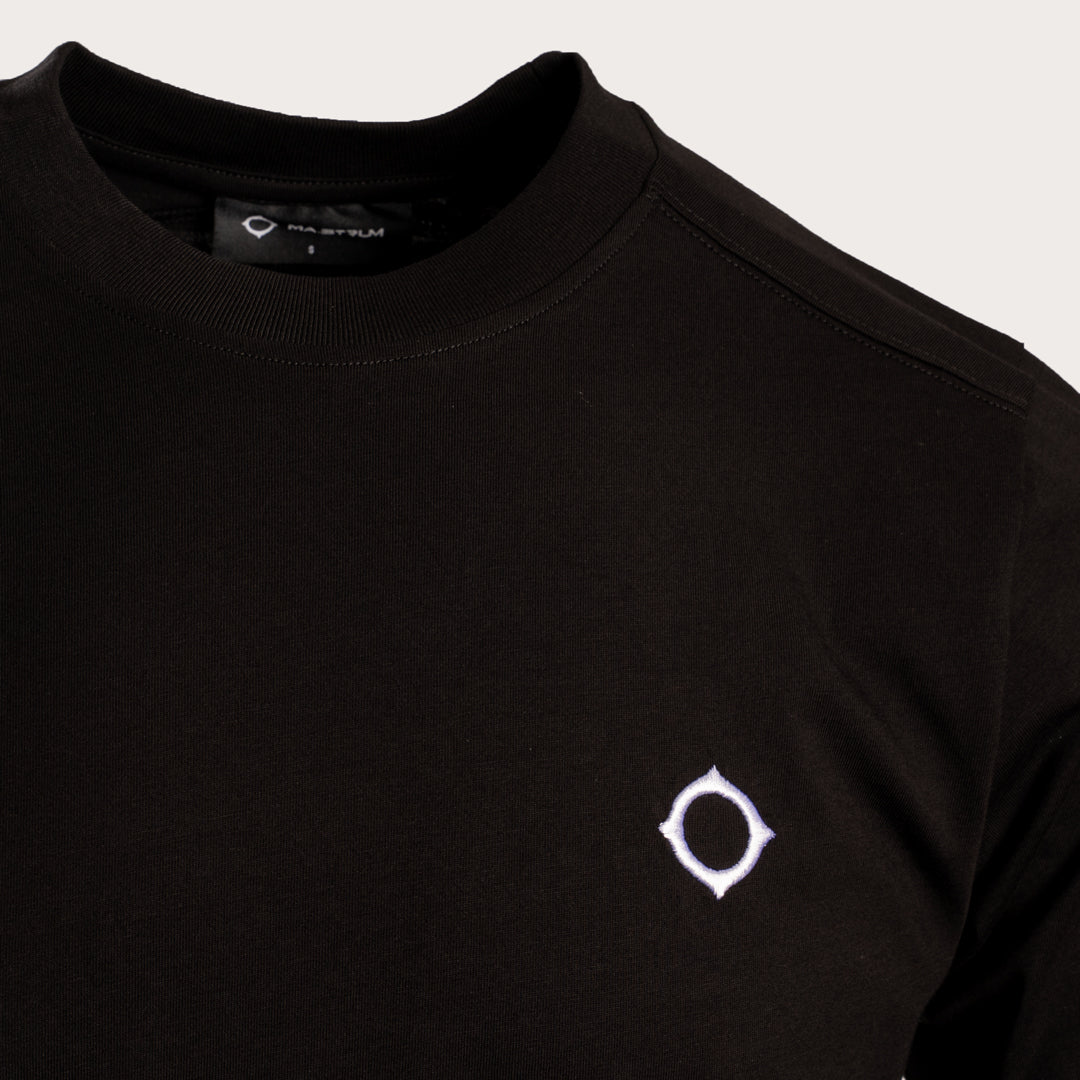 Close-up of a black crewneck sweatshirt featuring a small white geometric logo on the left chest, set against a light gray background. MA.Strum T-Shirt available at Sakks Menswear in Southampton