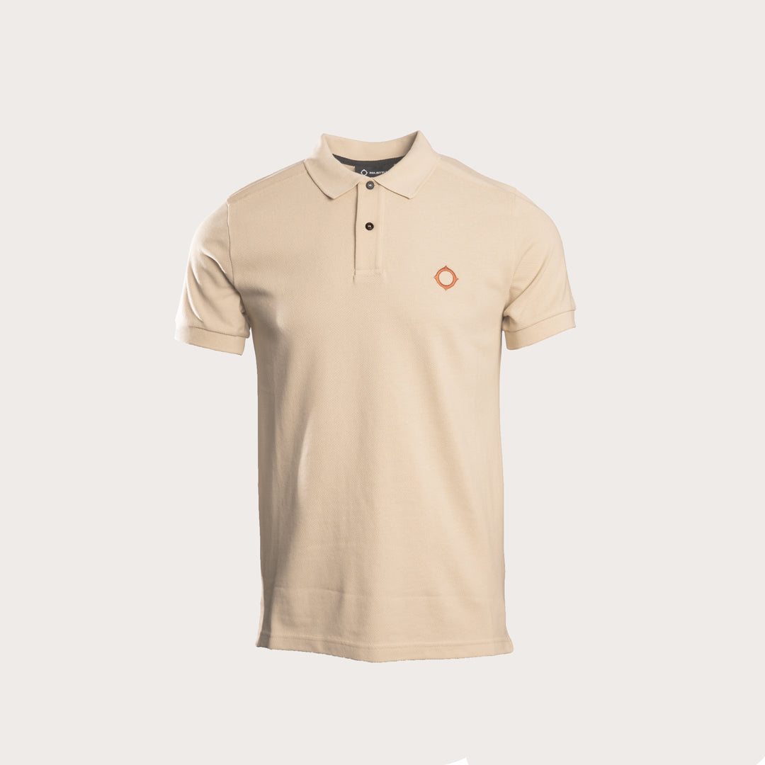A beige short-sleeve polo shirt with a two-button placket and a small orange circular logo on the left chest, displayed on a light gray background. MA.Strum Polo available at Sakks Menswear in Southampton.
