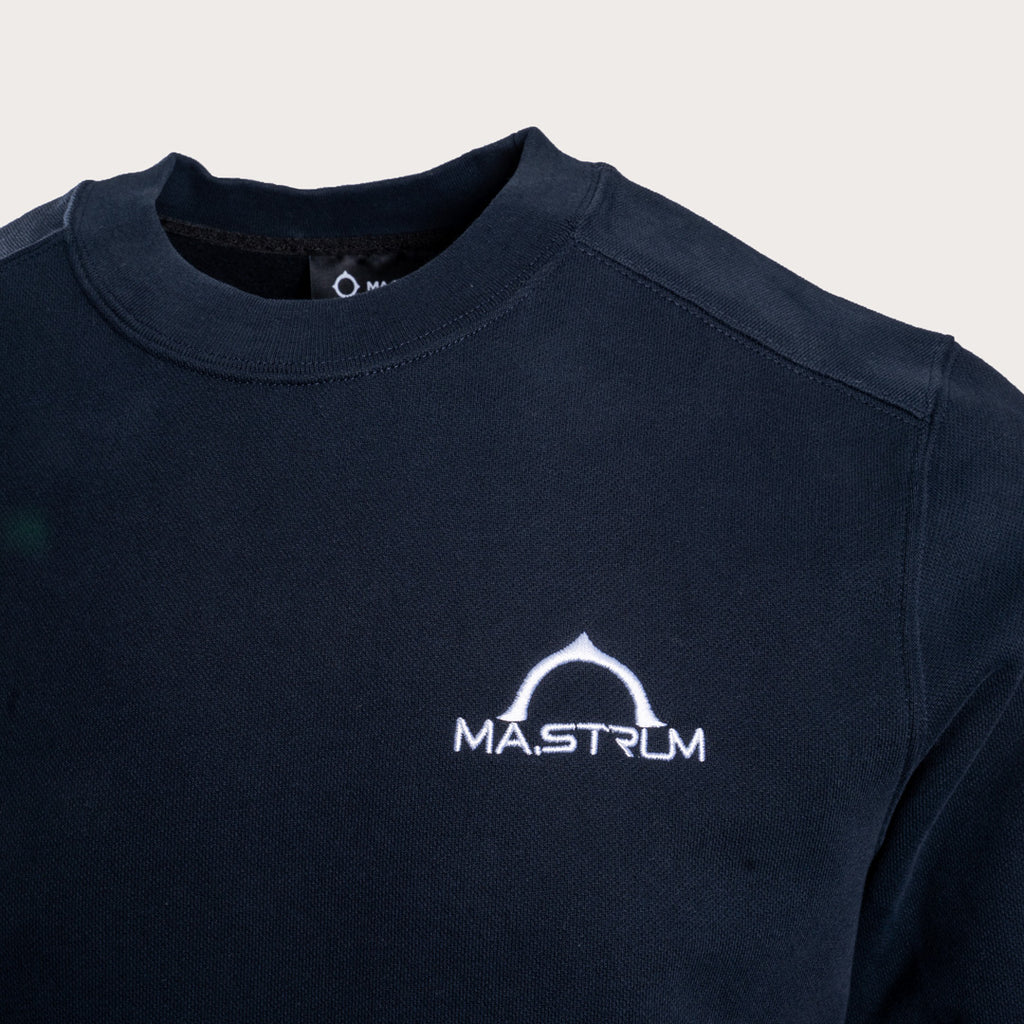 Close-up of a dark navy crewneck sweatshirt featuring a white printed 'MASTRUM' logo on the left chest, set against a light beige background. MA.Strum Sweatshirt available at Sakks Menswear in Southampton.