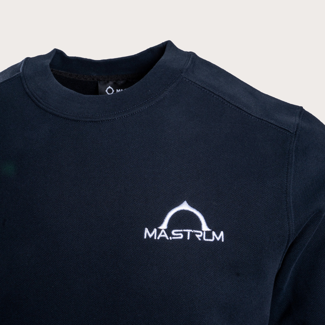 Close-up of a dark navy crewneck sweatshirt featuring a white printed 'MASTRUM' logo on the left chest, set against a light beige background. MA.Strum Sweatshirt available at Sakks Menswear in Southampton.