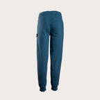 A pair of dark teal blue sweatpants shown from the back, featuring a small black brand patch on the left side, set against a solid light gray background. MA.Strum Sweat Pants available at Sakks Menswear in Southampton.