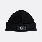 A black knit beanie hat with a folded cuff featuring a black rectangular patch with a white geometric target logo and four snap buttons. MA.Strum Beanie available at Sakks Menswear in Southampton.