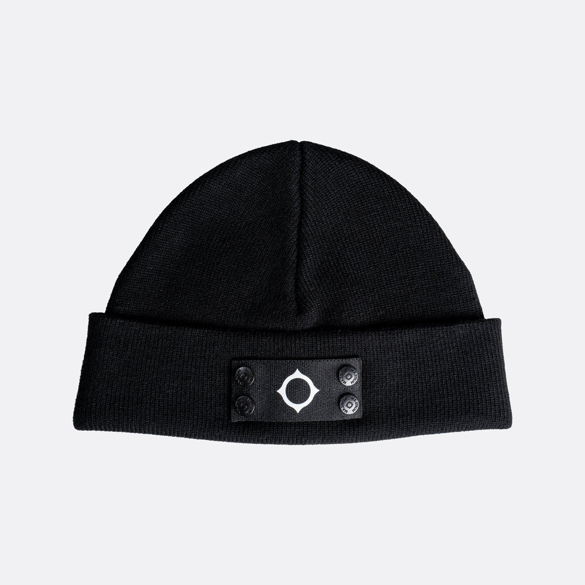 A black knit beanie hat with a folded cuff featuring a black rectangular patch with a white geometric target logo and four snap buttons. MA.Strum Beanie available at Sakks Menswear in Southampton.