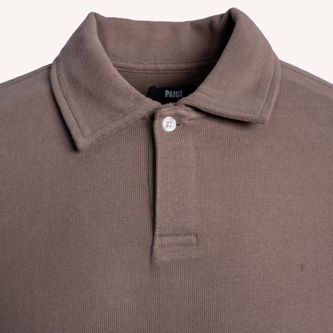 Close-up of a brown ribbed knit polo shirt collar with a single white button and a visible PAIGE neck label. PAIGE Polo available at Sakks Menswear in Southampton.