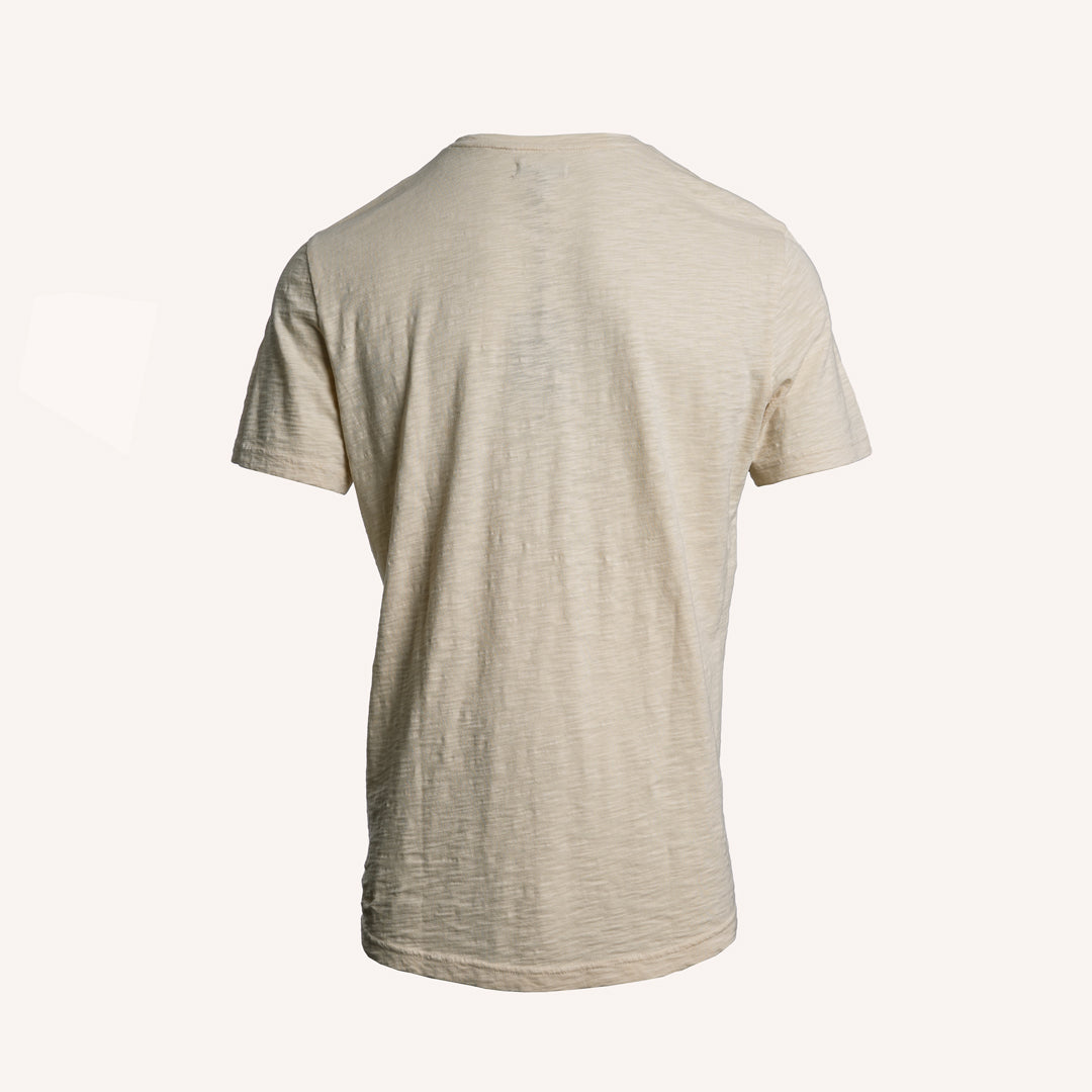 A short-sleeve crewneck t-shirt in a light beige or oatmeal heathered fabric, shown from the back against a solid off-white background. PAIGE T-Shirt available at Sakks Menswear in Southampton.