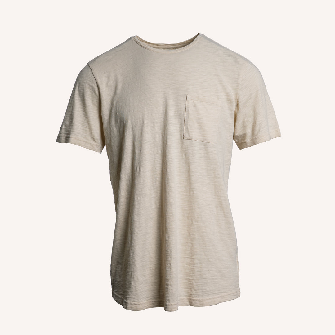 A light beige short-sleeve crewneck t-shirt with a single chest pocket, displayed against a solid off-white background. PAIGE T-Shirt available at Sakks Menswear in Southampton.