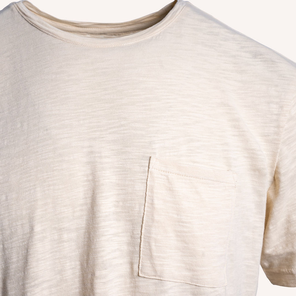 Close-up of a short-sleeve crewneck t-shirt in a light cream or off-white color, featuring a single chest pocket on the wearer's left side. PAIGE T-Shirt available at Sakks Menswear in Southampton.