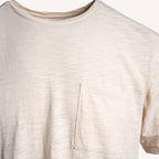 Close-up of a short-sleeve crewneck t-shirt in a light cream or off-white color, featuring a single chest pocket on the wearer's left side. PAIGE T-Shirt available at Sakks Menswear in Southampton.