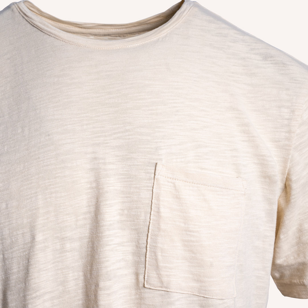 Close-up of a short-sleeve crewneck t-shirt in a light cream or off-white color, featuring a single chest pocket on the wearer's left side. PAIGE T-Shirt available at Sakks Menswear in Southampton.