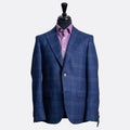 A blue and navy plaid blazer displayed on a black mannequin torso, layered over a purple dress shirt, against a light gray background. Sand Copenhagen Blazer available at Sakks Menswear in Southampton.