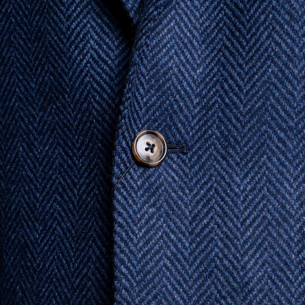 Close-up of a navy blue herringbone tweed fabric with a single metallic button on the front. Sand Copenhagen Blazer available at Sakks Menswear in Southampton.