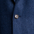 Close-up of a navy blue herringbone tweed fabric with a single metallic button on the front. Sand Copenhagen Blazer available at Sakks Menswear in Southampton.